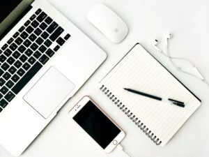 Minimalist workspace featuring laptop, smartphone, notebook, pen, and earbuds for productivity.